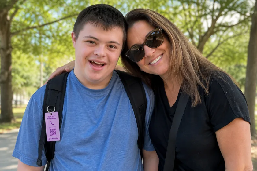 A smiling young man with his mother outdoors, a lavender PhoneTag contact tag clipped to his backpack strap